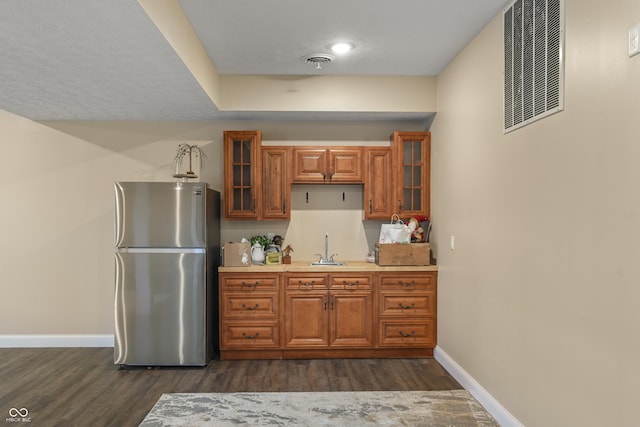 kitchen with brown cabinetry, freestanding refrigerator, visible vents, and a sink