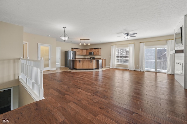 unfurnished living room featuring baseboards, dark wood finished floors, ceiling fan, a textured ceiling, and a sink