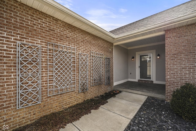 entrance to property with brick siding and a shingled roof