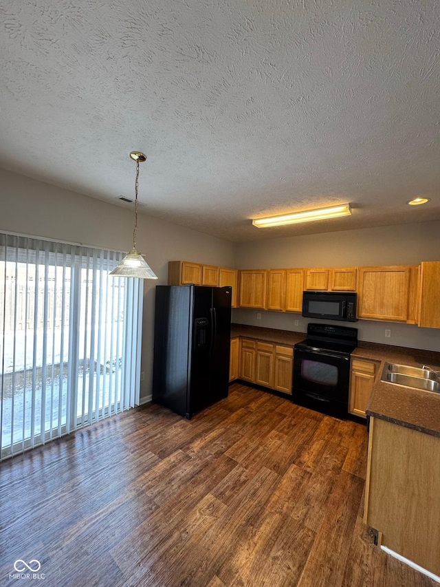 kitchen with dark countertops, dark wood-style floors, hanging light fixtures, black appliances, and a sink