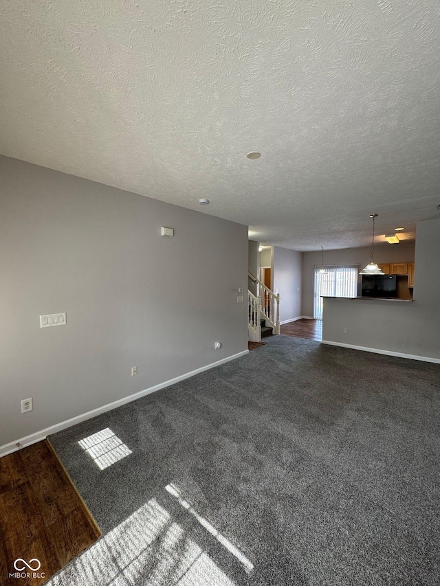 unfurnished living room with dark carpet, a textured ceiling, baseboards, and stairs