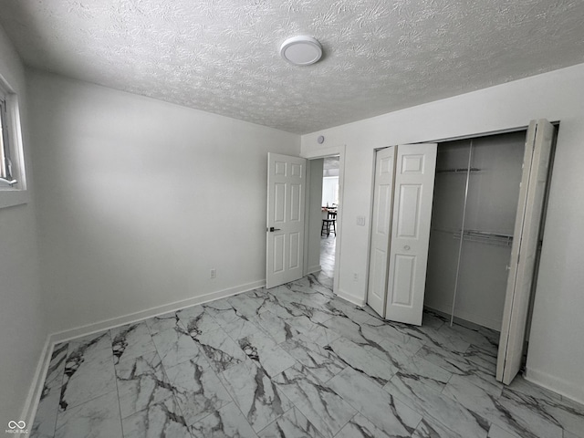 unfurnished bedroom featuring a closet, marble finish floor, a textured ceiling, and baseboards