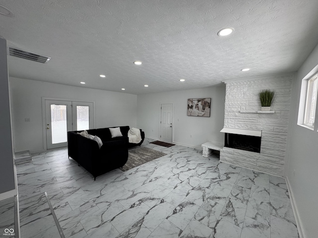 living area featuring marble finish floor, visible vents, a wealth of natural light, and a stone fireplace