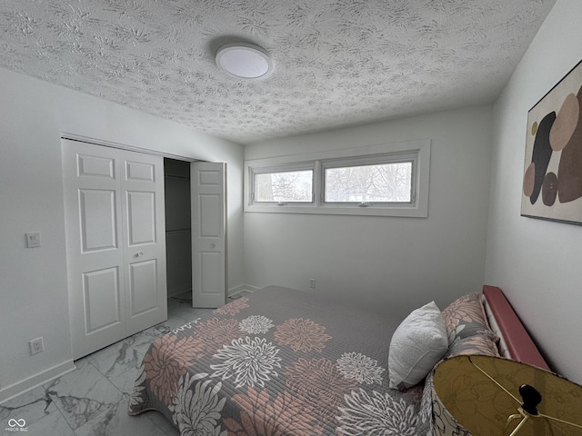 bedroom featuring a closet, marble finish floor, a textured ceiling, and baseboards