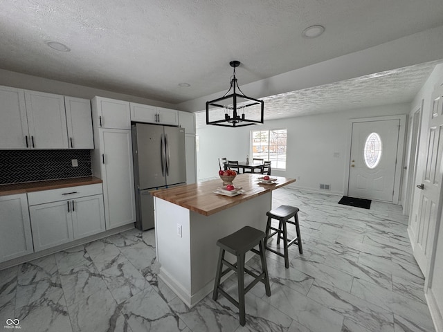 kitchen with wood counters, a kitchen breakfast bar, decorative light fixtures, freestanding refrigerator, and marble finish floor