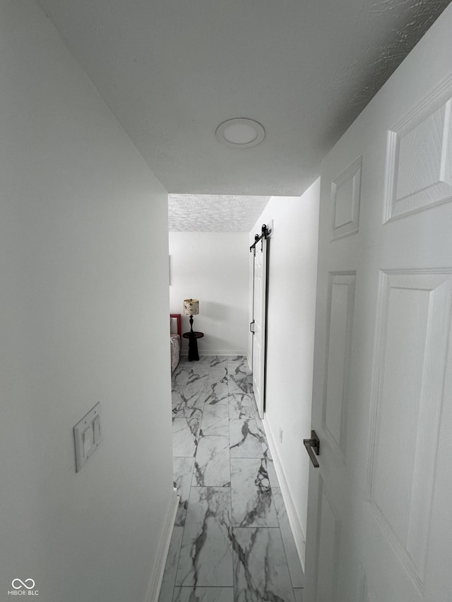 corridor featuring a textured ceiling, marble finish floor, a barn door, and baseboards