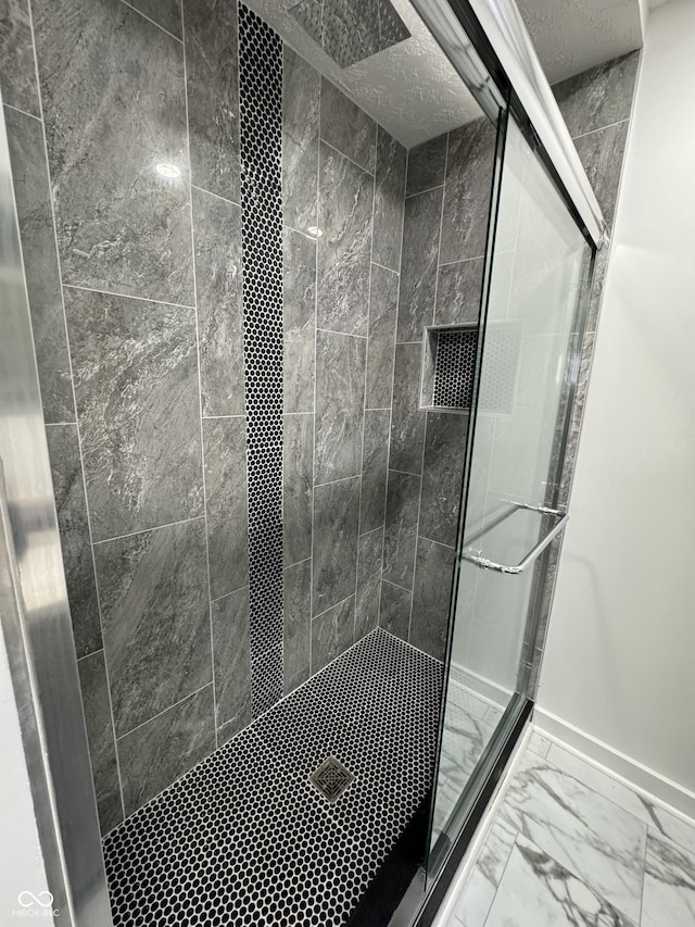 bathroom with marble finish floor, a shower stall, and baseboards