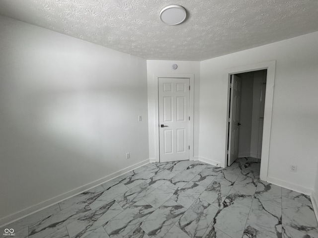 spare room featuring marble finish floor, baseboards, and a textured ceiling