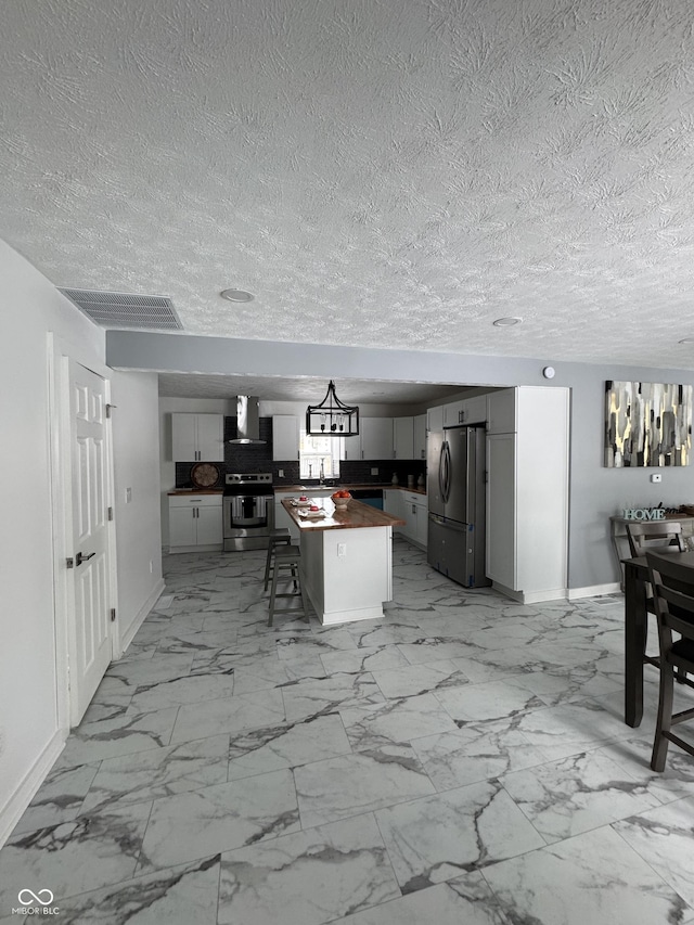 kitchen with visible vents, wall chimney exhaust hood, a kitchen island, appliances with stainless steel finishes, and wood counters