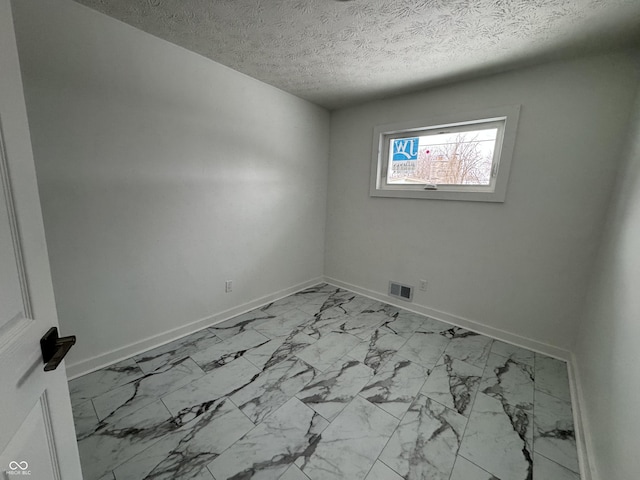 empty room featuring a textured ceiling, marble finish floor, visible vents, and baseboards