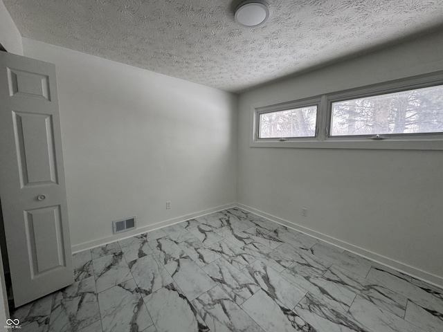 unfurnished room featuring a textured ceiling, marble finish floor, visible vents, and baseboards