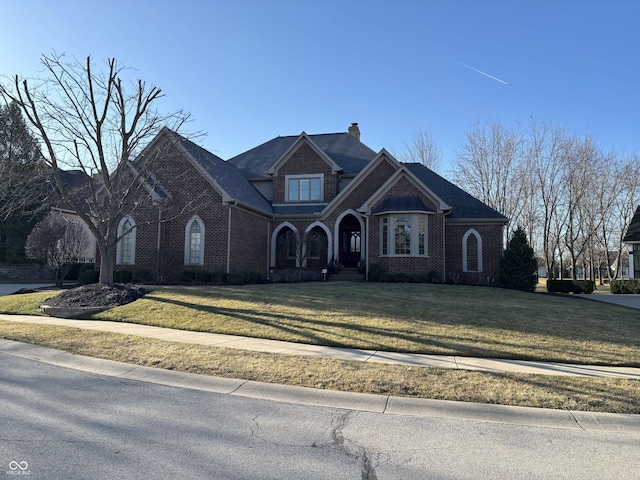 view of front of property featuring brick siding, a chimney, and a front lawn