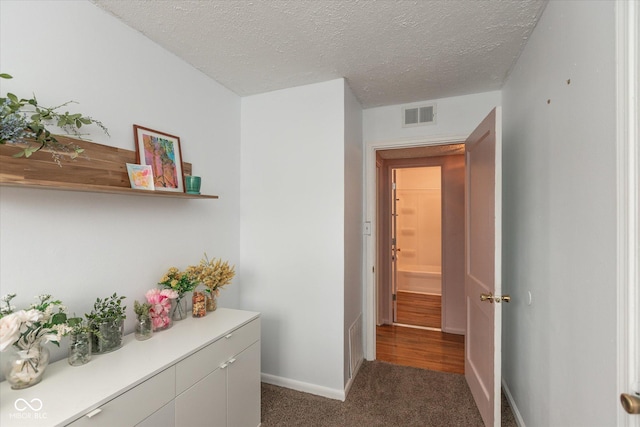 hallway with baseboards, visible vents, dark colored carpet, and a textured ceiling