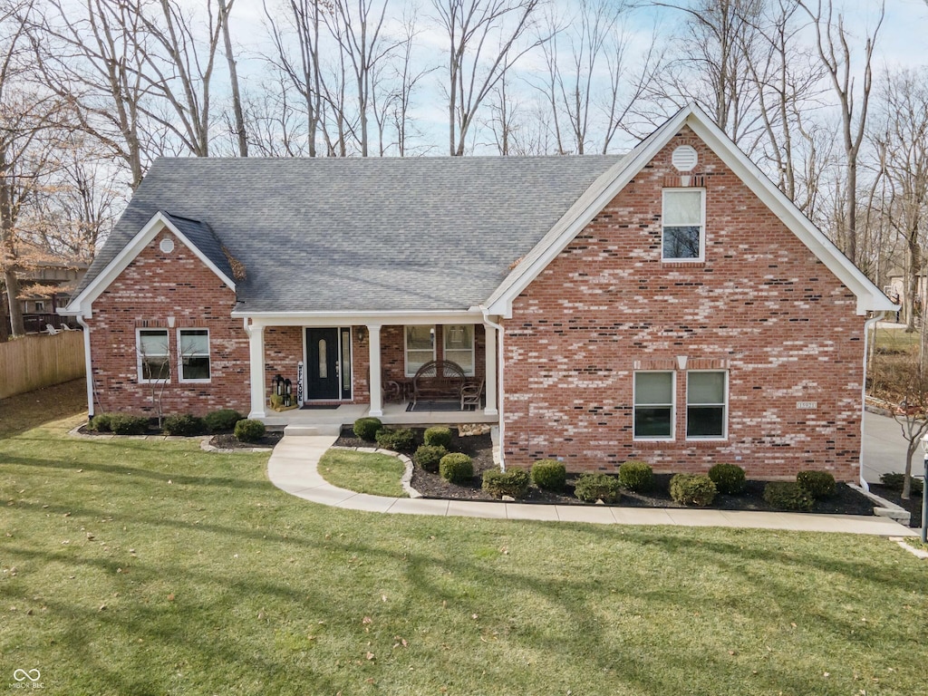 view of front facade with a shingled roof, a front yard, covered porch, and brick siding