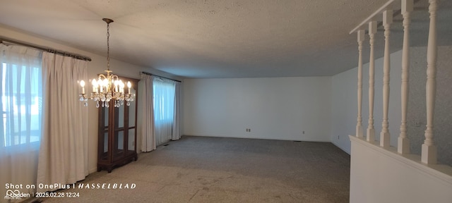 carpeted empty room featuring a healthy amount of sunlight, a chandelier, and a textured ceiling