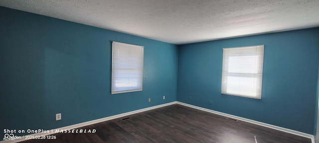 spare room with visible vents, a textured ceiling, baseboards, and wood finished floors