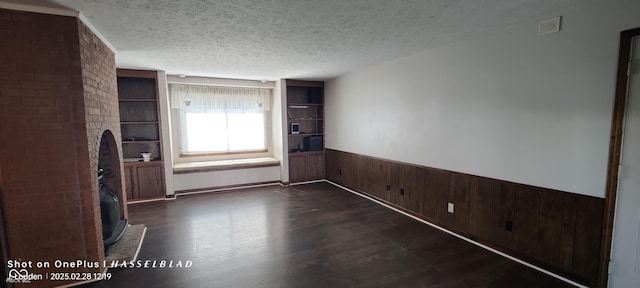 unfurnished living room featuring wooden walls, visible vents, wainscoting, and a textured ceiling