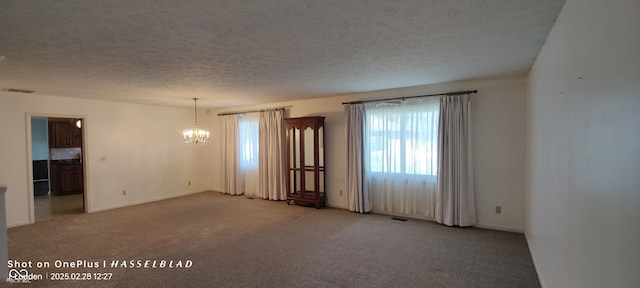 spare room featuring light carpet, an inviting chandelier, visible vents, and a textured ceiling