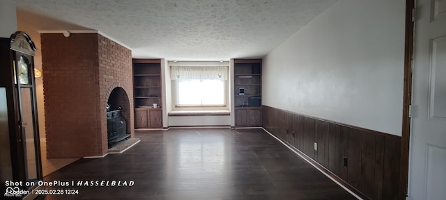 unfurnished living room with dark wood-style floors, wainscoting, a textured ceiling, and wooden walls