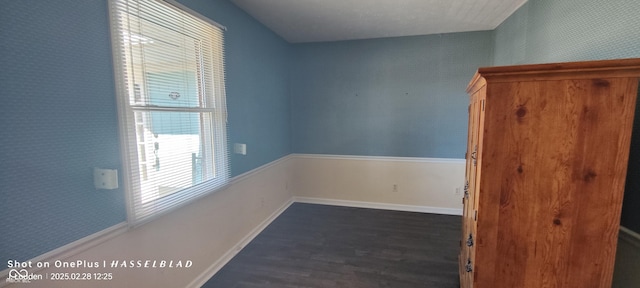 empty room with dark wood-type flooring, baseboards, and wallpapered walls