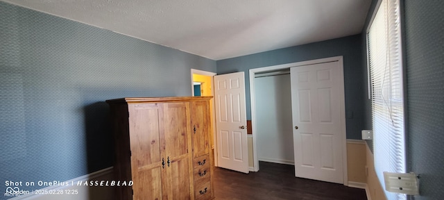 unfurnished bedroom with wallpapered walls, baseboards, dark wood finished floors, and a closet