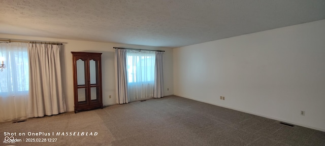 spare room featuring a textured ceiling, carpet flooring, visible vents, and baseboards