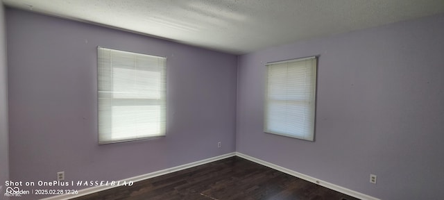 empty room with a textured ceiling, dark wood-style flooring, and baseboards