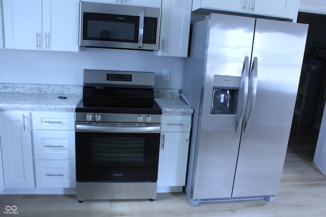 kitchen featuring appliances with stainless steel finishes, light wood-type flooring, white cabinets, and light stone counters