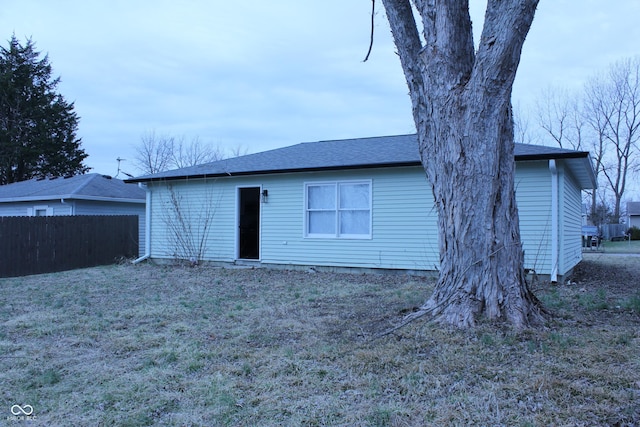 rear view of house featuring roof with shingles, fence, and a lawn