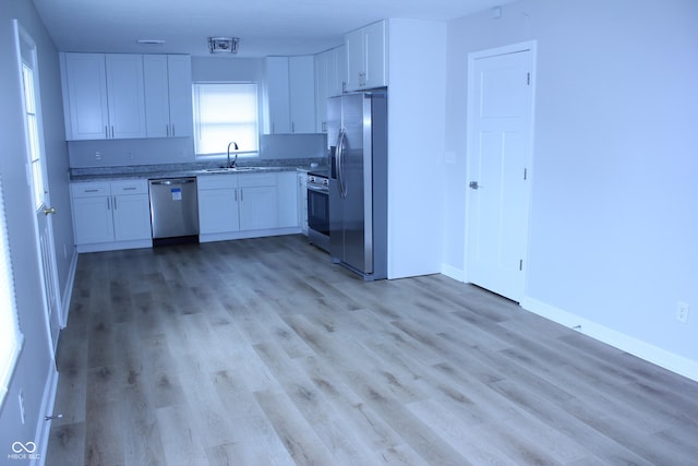 kitchen with appliances with stainless steel finishes, white cabinets, a sink, and light wood finished floors