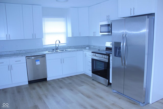 kitchen with appliances with stainless steel finishes, light wood-type flooring, white cabinetry, and a sink