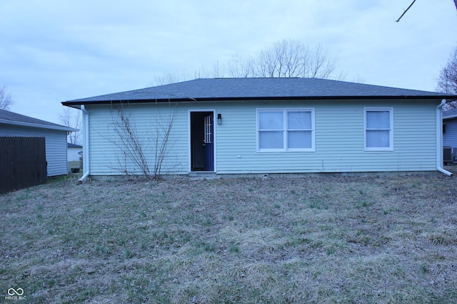 rear view of house with a shingled roof, a lawn, and central AC unit