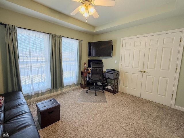 office space featuring a tray ceiling, carpet, a ceiling fan, and baseboards