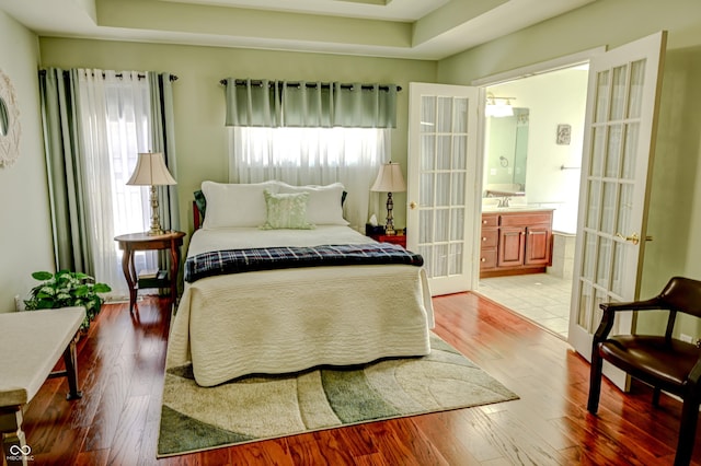 bedroom with light wood finished floors, connected bathroom, a tray ceiling, french doors, and a sink