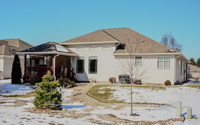 snow covered rear of property featuring covered porch and roof with shingles