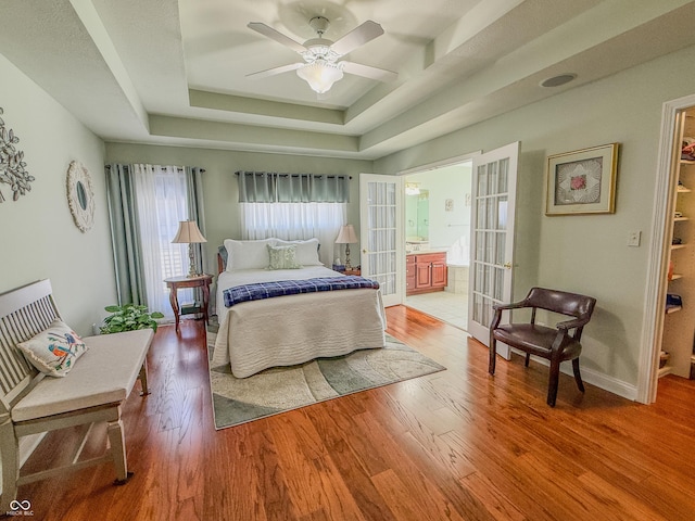 bedroom with french doors, a tray ceiling, wood finished floors, and baseboards