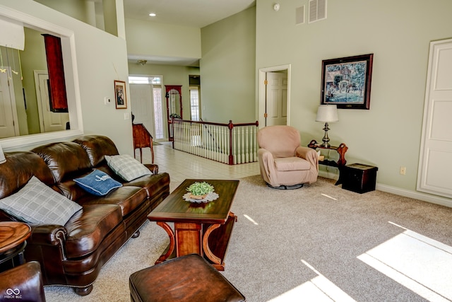 living room with light tile patterned floors, light carpet, a high ceiling, visible vents, and baseboards