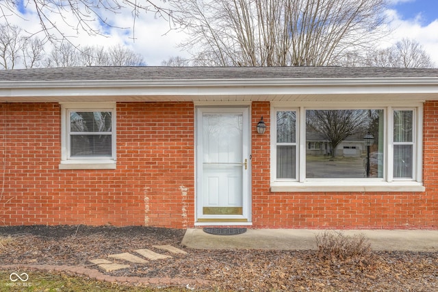 property entrance with roof with shingles and brick siding