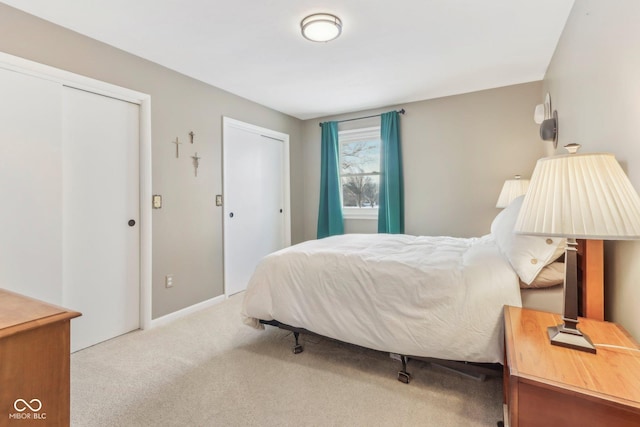 bedroom with baseboards, multiple closets, and light carpet