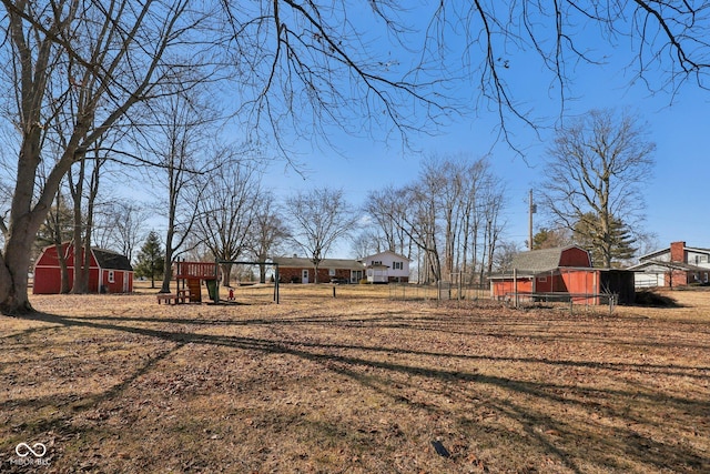 view of yard featuring a barn, fence, playground community, and an outdoor structure