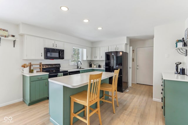 kitchen with a sink, black appliances, light wood-style floors, green cabinets, and a kitchen bar