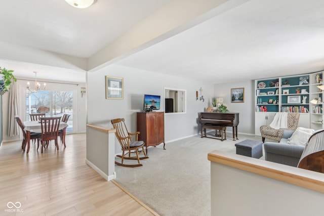 living area with beamed ceiling, baseboards, a chandelier, and light wood finished floors