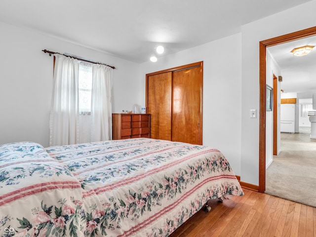 bedroom featuring freestanding refrigerator, a closet, baseboards, and hardwood / wood-style flooring