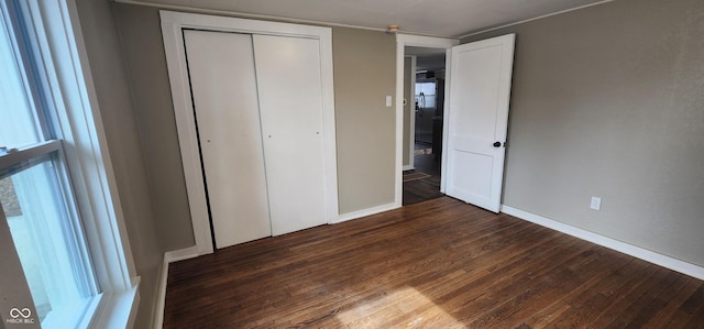 unfurnished bedroom featuring a closet, dark wood-style flooring, and baseboards