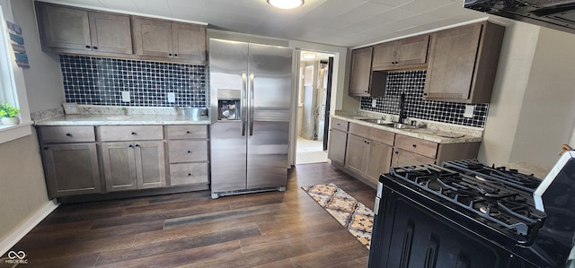 kitchen featuring stainless steel fridge, dark wood-style floors, light stone countertops, black gas stove, and a sink