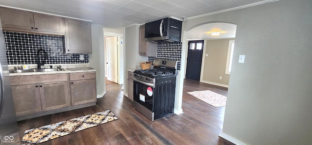 kitchen with arched walkways, stainless steel range with gas cooktop, dark wood-style flooring, backsplash, and a sink