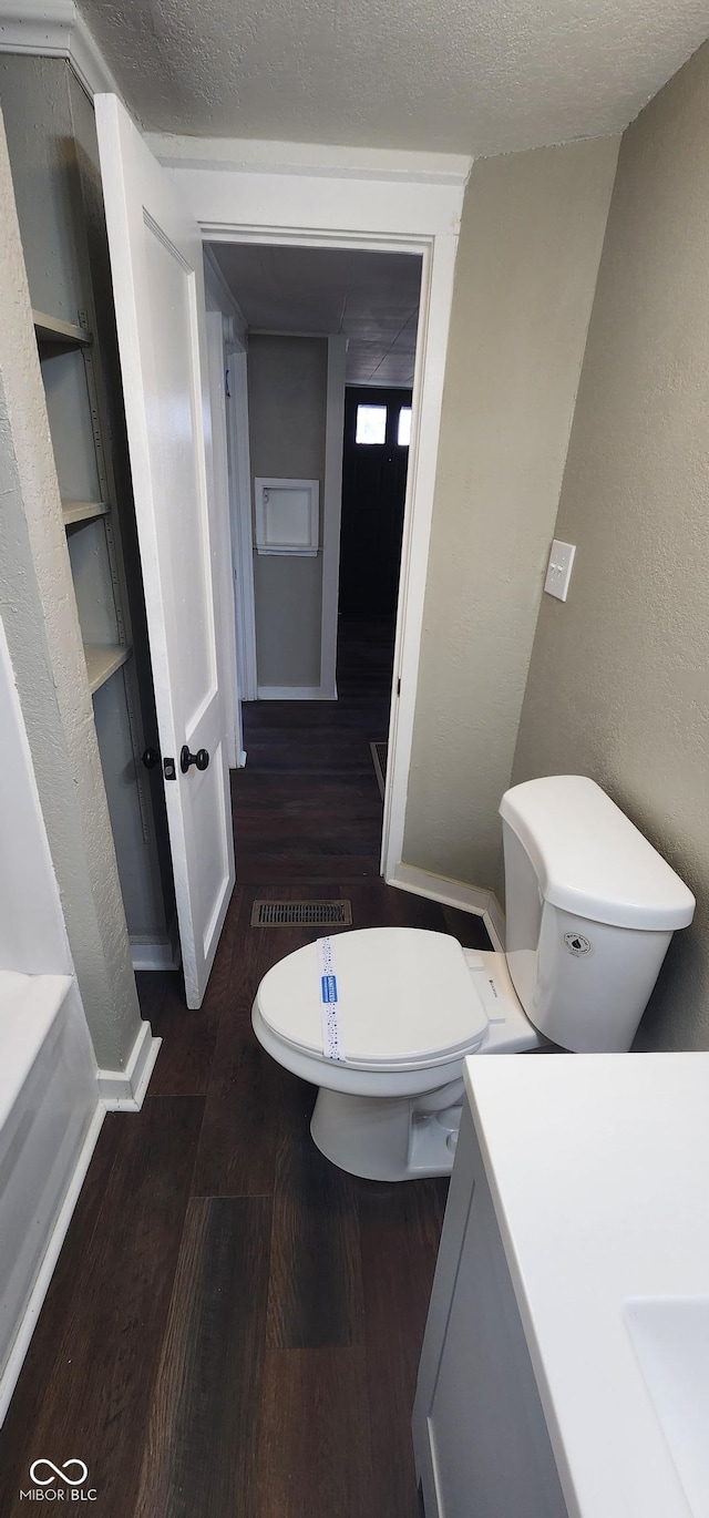 bathroom with a textured wall, toilet, wood finished floors, a textured ceiling, and vanity