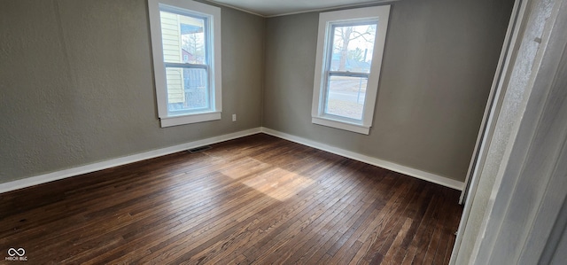 empty room with dark wood-type flooring, a healthy amount of sunlight, visible vents, and baseboards