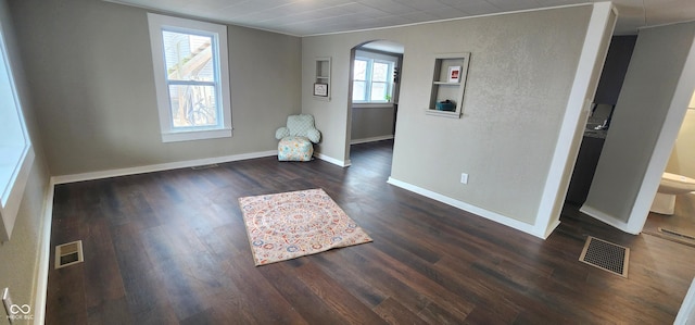 interior space with dark wood-style floors, baseboards, visible vents, and arched walkways