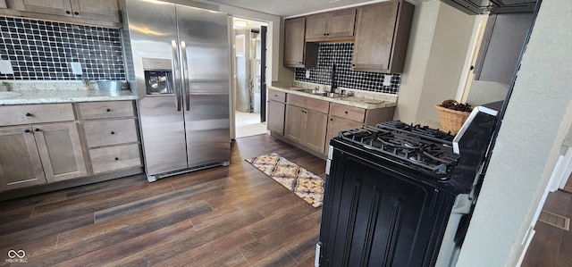 kitchen featuring gas range, dark wood-style flooring, light stone countertops, stainless steel refrigerator with ice dispenser, and a sink